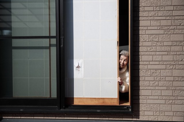 In this picture taken on January 16, 2018, Kimiko Nishimoto poses next to a picture of her on the sliding window of her house in the western Japanese city of Kumamoto. The madcap Japanese great-grandmother armed with a camera and an appetite for mischief has shot to fame for taking side-splitting selfies -- many of which appear to put her in harm's way. / AFP PHOTO / Behrouz MEHRI / TO GO WITH Japan-lifestyle-photography-offbeat-senior-citizens,FEATURE by Alistair HIMMER