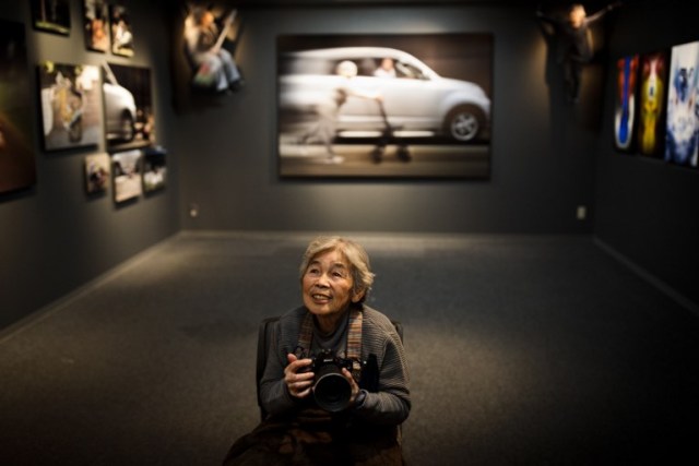 In this picture taken on December 14, 2017, Kimiko Nishimoto poses with a camera in the opening day of her photo exhibition in Tokyo. The madcap Japanese great-grandmother armed with a camera and an appetite for mischief has shot to fame for taking side-splitting selfies -- many of which appear to put her in harm's way. / AFP PHOTO / Behrouz MEHRI / TO GO WITH Japan-lifestyle-photography-offbeat-senior-citizens,FEATURE by Alistair HIMMER