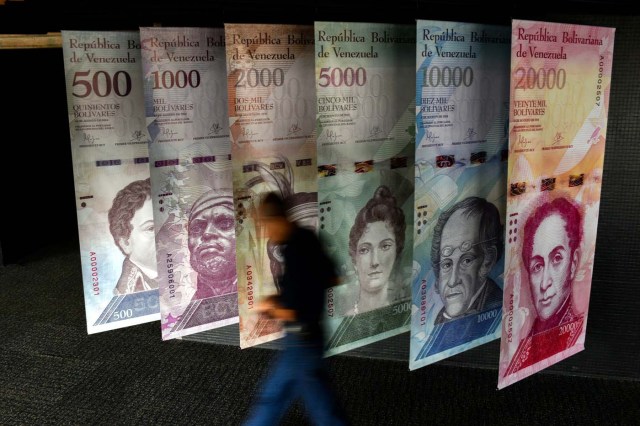 A man walks past banners showing banners depicting Venezuela's currency, the Bolivar, at the Central Bank of Venezuela (BCV) in Caracas on January 31, 2018. Venezuelan President Nicolas Maduro signed the proposal of a new digital currency called "Petro" to try to combat the economic crisis. / AFP PHOTO / FEDERICO PARRA