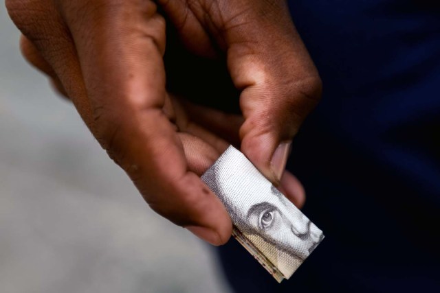 Wilmer Rojas, 25, holds a folded Bolivar bill, which he uses to make crafts in Caracas on January 30, 2018. A young Venezuelan tries to make a living out of devalued Bolivar banknotes by making crafts with them. / AFP PHOTO / FEDERICO PARRA