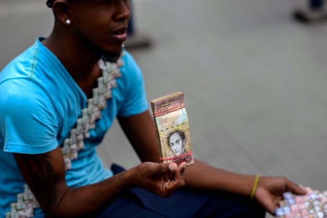 Wilmer Rojas, 25, holds a wad of Bolivar bills, which he uses to make crafts in Caracas on January 30, 2018. A young Venezuelan tries to make a living out of devalued Bolivar banknotes by making crafts with them. / AFP PHOTO / FEDERICO PARRA