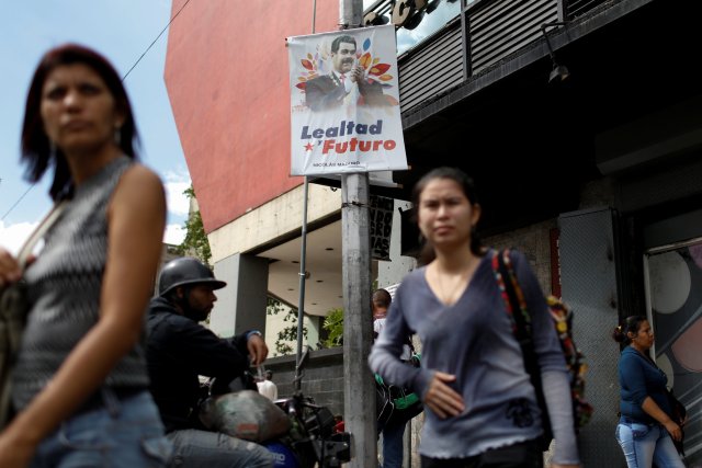 People walk past a banner depicting Venezuela's President Nicolas Maduro that reads "Loyalty and future" in downtown Caracas, Venezuela February 1, 2018. Picture taken February 1, 2018. REUTERS/Marco Bello
