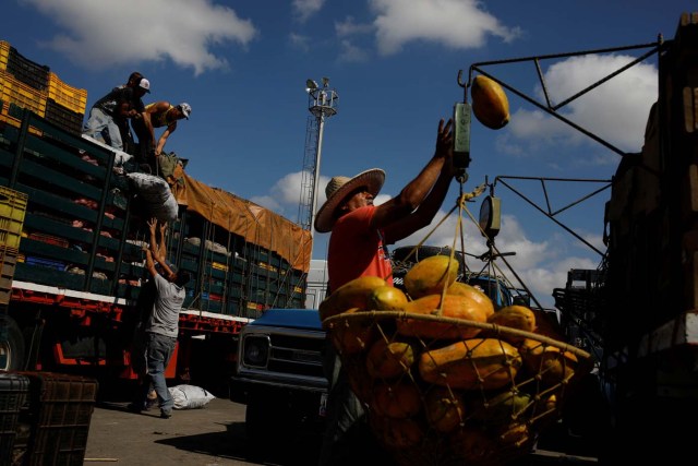 Workers load merchandise into Humberto Aguilar's truck next to a papaya seller at the wholesale market in Barquisimeto, Venezuela January 30, 2018. REUTERS/Carlos Garcia Rawlins SEARCH "LAWLESS ROADS" FOR THIS STORY. SEARCH "WIDER IMAGE" FOR ALL STORIES.?