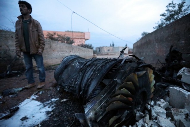 A picture taken on February 3, 2018, shows a Syrian man standing next to a burnt jet engine at the site of a downed Sukhoi-25 fighter jet near the Syrian city of Saraqib, southwest of Aleppo. Rebel fighters shot down a Russian plane over Syria's northwest Idlib province and captured its pilot, the Syrian Observatory for Human Rights said. / AFP PHOTO / OMAR HAJ KADOUR