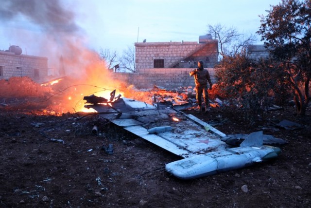 A picture taken on February 3, 2018, shows a Rebel fighter taking a picture of a downed Sukhoi-25 fighter jet near the Syrian city of Saraqib, southwest of Aleppo. Rebel fighters shot down a Russian plane over Syria's northwest Idlib province and captured its pilot, the Syrian Observatory for Human Rights said. / AFP PHOTO / OMAR HAJ KADOUR