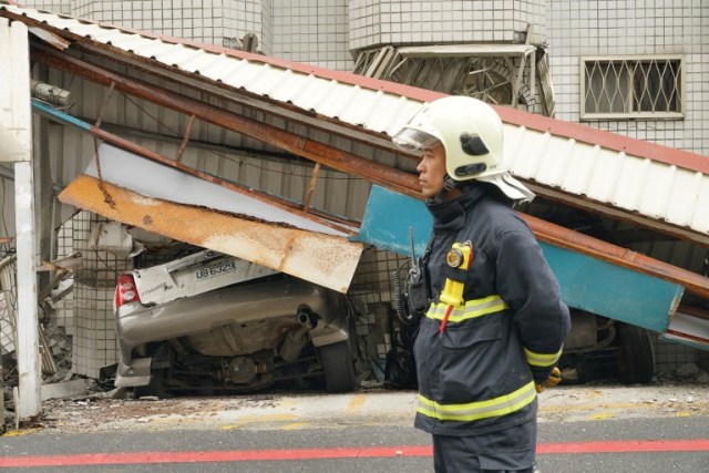 Un trabajador de rescate se para junto a un automóvil aplastado (L) la mañana después de que un terremoto de magnitud 6,4 golpeara la ciudad oriental taiwanesa de Hualien, el 7 de febrero de 2018. / AFP PHOTO / PAUL YANG