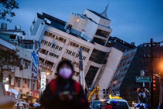 Un peatón camina por una carretera principal mientras el edificio Yun Tsui (parte posterior C) se inclina hacia un lado después de un terremoto durante la noche en la ciudad taiwanesa de Hualien el 7 de febrero de 2018. / AFP PHOTO / Anthony WALLACE
