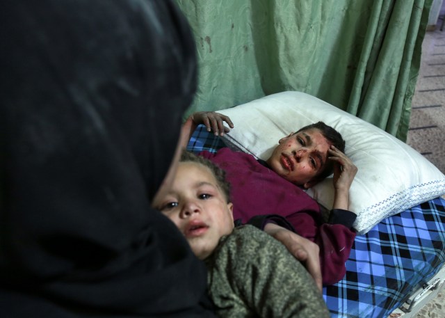 A Syrian boy sits on a bed as a woman carries a child above him as they arrive for medical attention at a make-shift clinic in the rebel-held town of Douma, in the besieged Eastern Ghouta region on the outskirts of the capital Damascus, following reported regime bombardment on the area on February 24, 2018. / AFP PHOTO / HAMZA AL-AJWEH