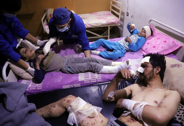 Doctors tend to ten-year-old Omar who was injured in an air strike that killed several members of his family on their home in Otaybah, in Syria's rebel-held enclave of Eastern Ghouta, as his father and seven-year-old sister, Manar, watch on at a make-shift hospital on February 25, 2018.  / AFP PHOTO / AMER ALMOHIBANY