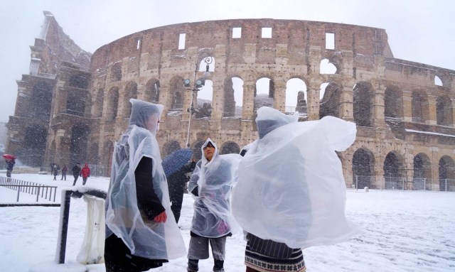 Japanese tourists put plastic coats as they visit the ancient Colosseum during a snowfall in Rome on February 26, 2018. / AFP PHOTO / Vincenzo PINTO