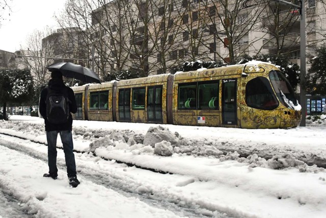 A man walks on a snow covered road past a tramway blocked by snow on March 1, 2018 in Montpellier, southern France, after heavy snow fall. Fresh heavy snowfalls and icy blizzards were expected to lash Europe on March 1 as the region shivers in a deadly deep-freeze that has gripped countries from the far north to the Mediterranean south. / AFP PHOTO / PASCAL GUYOT