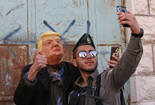 An Israeli soldier takes a selfie with an Israeli settler dressed in a mask of US President Donald Trump as they celebrate the Jewish Purim holiday at al-Shuhada street in the divided West Bank town of Hebron, on March 01, 2018. / AFP PHOTO / HAZEM BADER