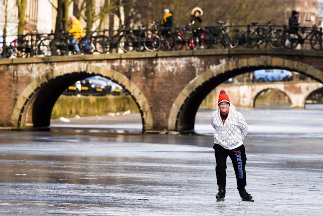 A skater skates on the ice of the lightly frozen Keizersgracht Canal in Amsterdam on March 1, 2018. Heavy snowfall and deadly blizzards lashed Europe, forcing airports to cancel or delay flights around the continent, as a deep freeze gripped countries from the far north to the Mediterranean beaches in the south. / AFP PHOTO / ANP / Evert Elzinga / Netherlands OUT