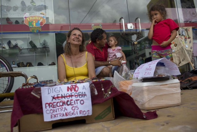 Una mujer brasileña vende bijouteries de artesanía con un letrero que dice "Di no a la xenofobia: prejuicio contra los extranjeros" en una feria callejera en la ciudad de Boa Vista, Roraima, Brasil, el 25 de febrero de 2018. Cuando el flujo migratorio venezolano estalló en 2017, la ciudad de Boa Vista, capital del estado de Roraima, a 200 kilómetros de la frontera con Venezuela, comenzó a establecer refugios a medida que la gente comenzaba a establecerse en plazas, parques y rincones de esta ciudad de 330,000 habitantes habitantes de los cuales el 10 por ciento es ahora venezolano. / AFP PHOTO / Mauro PIMENTEL