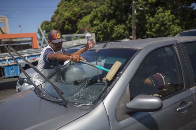 Carlos, a Venezuelan immigrant who arrived two months ago searching for a job to send money for the rest o the family who stayed in Venezuela, washes window cars on a traffic stop in the city of Boa Vista, Roraima, Brazil, on February 27, 2018. When the Venezuelan migratory flow exploded in 2017 the city of Boa Vista, the capital of the state of Roraima, 200 kilometers from the Venezuelan border, began to set up shelters as people started to settle in squares, parks and corners of this city of 330,000 inhabitants of which 10 percent is now Venezuelan. / AFP PHOTO / MAURO PIMENTEL