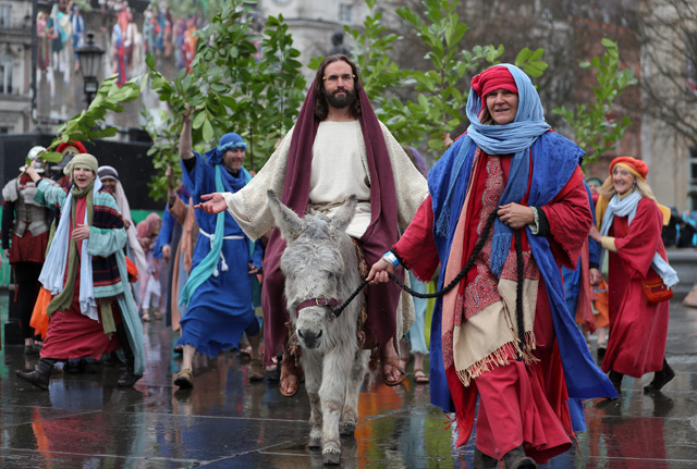 Actor James Burke-Dunsmore (C) arrives on a donkey as he plays the role of Jesus Christ, during a performance of Wintershall's 'The Passion of Jesus' on Good Friday in Trafalgar Square in London on March 30, 2018.  The Passion of Jesus tells the story from the Bible of Jesus's visit to Jerusalem and his crucifixion. On Good Friday 20,000 people gather to watch the Easter story in central London. One hundred Wintershall players bring their portrayal of the final days of Jesus to this iconic location in the capital. / AFP PHOTO / Daniel LEAL-OLIVAS