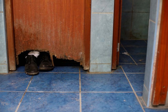 The shoes of Alvaro Betancourt, who is traveling by bus from Caracas to Chile, are seen through a hole in a door while he takes a shower at a bus station in Tumbes, Peru, November 11, 2017. Carlos Garcia Rawlins: "At the bus terminal in Tumbes the bathroom was in a bad state of repair; the toilets were dirty and didn't work properly, the floor and walls of the showers were covered in fungus, to the point that someone placed a piece of wood on the floor so they could stand under the water without touching the floor. But after several days without bathing, the conditions of the bathroom were not so important, so one by one, most of the travelers took a shower before continuing on the road". REUTERS/Carlos Garcia Rawlins SEARCH "RAWLINS BUS" FOR THIS STORY. SEARCH "WIDER IMAGE" FOR ALL STORIES.