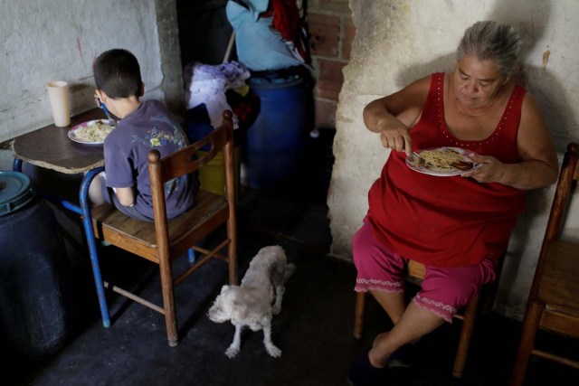 Antonia Torres (R) y Luis, hijo de su hija Yuni Pérez, comen pasta recibida en una caja de CLAP, una donación del gobierno venezolano de alimentos básicos, en su casa en el barrio pobre de Petare en Caracas, Venezuela el 9 de marzo de 2018. Fotografía tomada el 9 de marzo de 2018. REUTERS / Marco Bello
