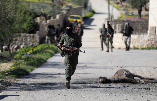 A Turkish-backed Free Syrian Army fighter runs next to the carcass of a dead animal north of Afrin, Syria March 17, 2018. REUTERS/Khalil Ashawi