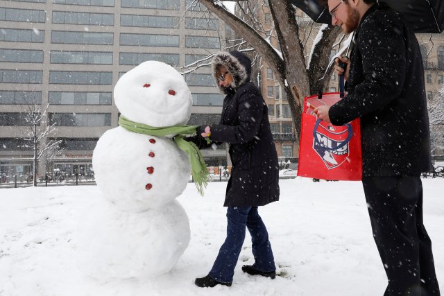 Stephen Shapanka looks on as Jeannie Boehne wears a scarf on a snowman during a snowstorm in Washington, U.S., March 21, 2018. REUTERS/Yuri Gripas
