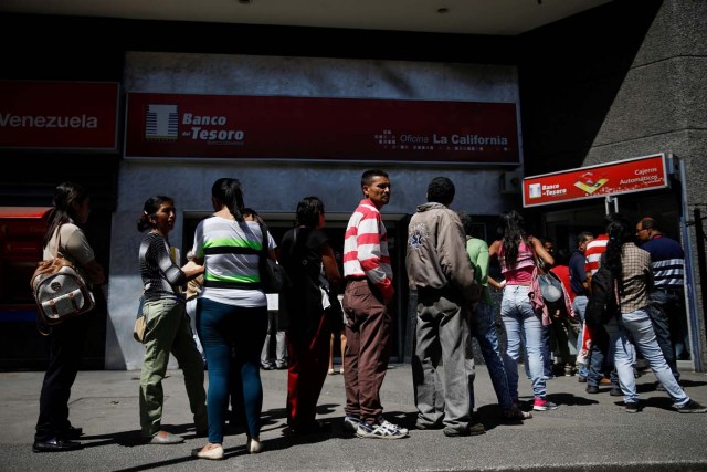 People stand in a queue to withdraw cash from an automated teller machine (ATM) outside a Banco del Tesoro branch in Caracas, Venezuela March 23, 2018. REUTERS/Carlos Garcia Rawlins