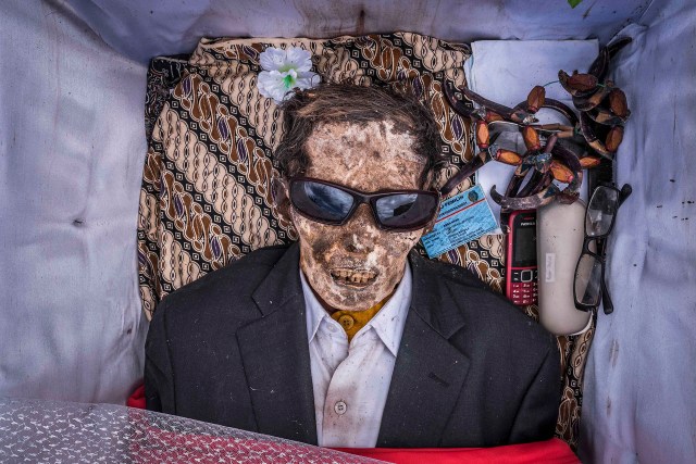 PIC BY Claudio Sieber / CATERS NEWS - (PICTURED Grandpa Ne Pua, passed away with 85 years. He has been buried in his favorite suit, together with hes favourite belongings, like the mobile phone and glasses.)THESE images show a unique insight into the village where the living dig up their dead relatives to clean their bones and to dress them up. The dead can even remain in homes for decades until the family throw a huge party in their honour. The corpses are treated as sick until they finally find peace after funeral rites known as Rambu Solo The bizarre ritual was pictured in South Sulawesi, Indonesia, where even buried relatives are taken out of their coffins for new outfits and a bone polish. SEE CATERS COPY