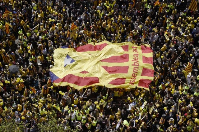 People carry a big Catalan pro-independence 'estelada' flag with a yellow ribbon on it during a demonstration to support Catalan pro-independence jailed leaders and politicians and called by 'Espai Democracia i Convivencia' platform that groups separatist collectives and unions in Barcelona on April 15, 2018.  Thousands of people marched in Barcelona today to protest the jailing of nine Catalan separatist leaders facing trial on "rebellion" charges. Many chanted "Freedom for the political prisoners" as they massed on the Parallel Avenue, one of the city's main streets, wearing yellow scarves, sweaters or jackets -- the colour chosen to show solidarity with the jailed leaders.  / AFP PHOTO / Josep LAGO