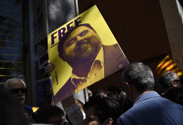A person holds up a placard with a portrait of jailed former Catalan vice-president Oriol Junqueras during a demonstration to support Catalan pro-independence jailed leaders and politicians and called by 'Espai Democracia i Convivencia' platform that groups separatist collectives and unions in Barcelona on April 15, 2018.  Thousands of people marched in Barcelona today to protest the jailing of nine Catalan separatist leaders facing trial on "rebellion" charges. Many chanted "Freedom for the political prisoners" as they massed on the Parallel Avenue, one of the city's main streets, wearing yellow scarves, sweaters or jackets -- the colour chosen to show solidarity with the jailed leaders.  / AFP PHOTO / Josep LAGO