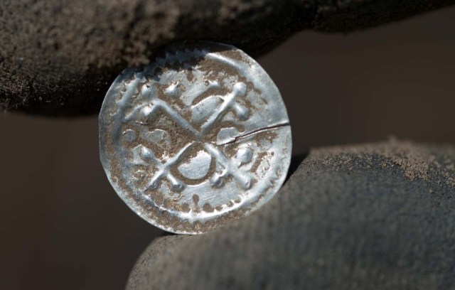 An archaeologist holds Denmark's first independent type of coin after its excavation in Schaprode, northern Germany on April 13, 2018. A 13-year-old boy and a hobby archaeologist have unearthed a "significant" trove in Germany which may have belonged to the legendary Danish king Harald Bluetooth who brought Christianity to Denmark. A dig covering 400 square metres (4,300 square feet) that finally started over the weekend by the regional archaeology service has since uncovered a trove believed linked to the Danish king who reigned from around 958 to 986. Braided necklaces, pearls, brooches, a Thor's hammer, rings and up to 600 chipped coins were found, including more than 100 that date back to Bluetooth's era.  / AFP PHOTO / dpa / Stefan Sauer / Germany OUT