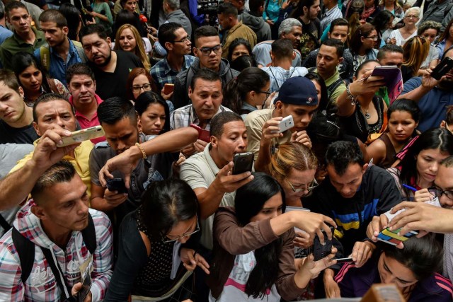 Venezuelans take pictures of the list of requirements to apply for a "Democratic Responsibility Visa" on display outside the Chilean consulate in Caracas, on April 16, 2018. Chilean President Sebastian Pinera announced on April 8 that Chile would ease visa regulations for Venezuelans fleeing the political crisis. In light of the "grave democratic crisis" gripping Venezuela, Pinera said he was creating a so-called visa of "democratic responsibility" which Venezuelan citizens could obtain through the Chilean embassy in Caracas.  / AFP PHOTO / Luis ROBAYO