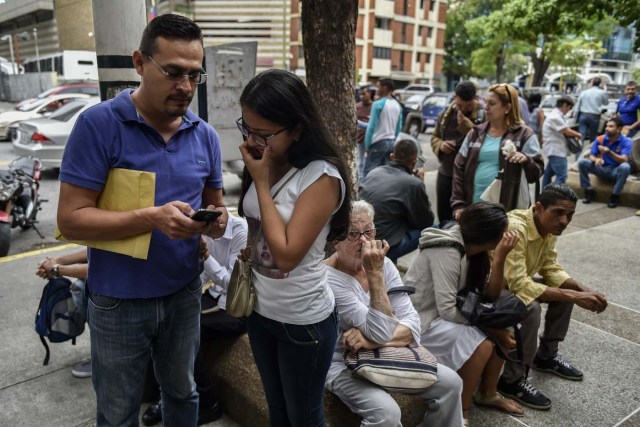 Venezuelans read the requirements needed to apply for a "Democratic Responsibility Visa" on their mobile phones, after taking pictures of the list put on display outside the Chilean consulate in Caracas, on April 16, 2018. Chilean President Sebastian Pinera announced on April 8 that Chile would ease visa regulations for Venezuelans fleeing the political crisis. In light of the "grave democratic crisis" gripping Venezuela, Pinera said he was creating a so-called visa of "democratic responsibility" which Venezuelan citizens could obtain through the Chilean embassy in Caracas. / AFP PHOTO / Luis ROBAYO