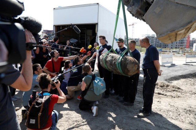 A member of German police answers journalists' questions next to a bomb dropped during World War II as it is lifted with a digger during the disposal operation on April 20, 2018 in Berlin. Thousands of people around Berlin's central railway station were evacuated as bomb disposal experts defused an unexploded World War II explosive unearthed on a building site in Berlin's Mitte district. / AFP PHOTO / Odd ANDERSEN