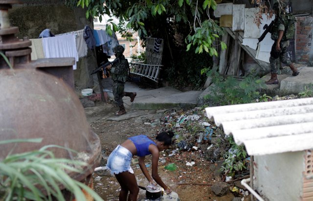 A youth washes dishes as Brazilian Armed Forces members patrol, during an operation against drug gangs, in the Lins slums complex in Rio de Janeiro, Brazil March 27, 2018.  REUTERS/Ricardo Moraes