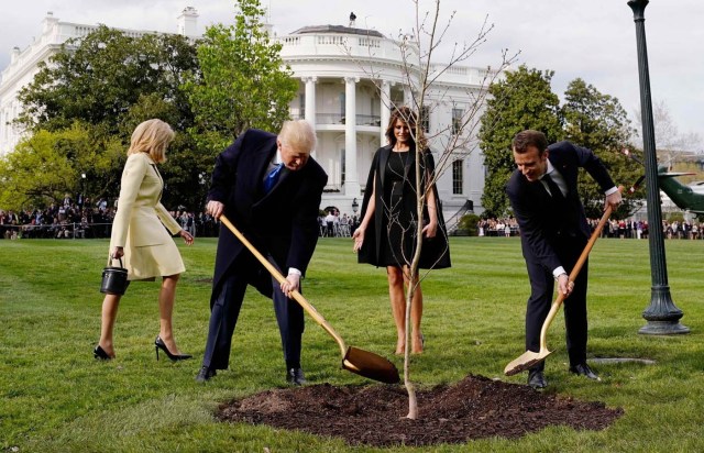 U.S. President Donald Trump and French President Emmanuel Macron shovel dirt onto a freshly planted oak tree as first lady Melania Trump and Brigitte Macron watch on the South Lawn of the White House in Washington, U.S., April 23, 2018. REUTERS/Joshua Roberts