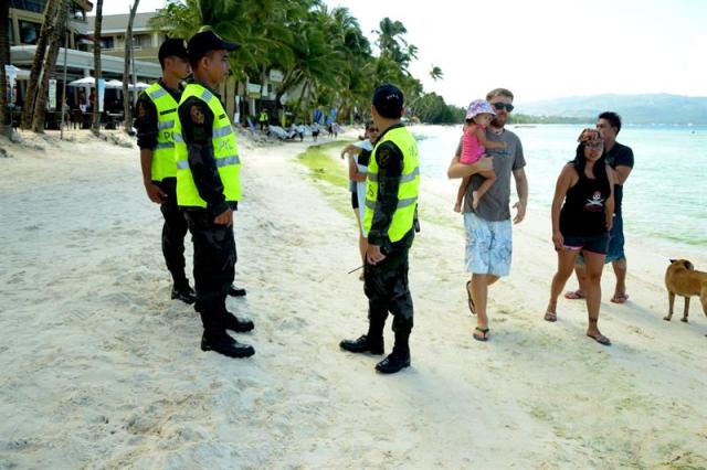 Turistas pasan junto a tres policías filipinos en la isla de Boracay, uno de los principales destinos turísticos de Filipinas, después de que cerrase al público por un plazo de seis meses en una polémica decisión del presidente, Rodrigo Duterte, en Boracay (Filipinas), hoy, 26 de abril de 2018. EFE/ Jo Haresh Tanodra