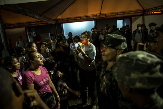 La trabajadora de una ONG organiza a cientos de venezolanos para repartir una cena de arroz y pollo, preparada por militares brasileños, en un estadio de fútbol que sirve como refugio temporal en Boa Vista. Credit Meridith Kohut para The New York Times