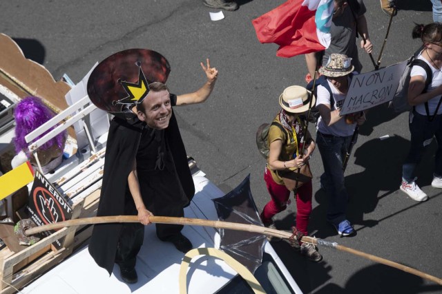 A man rides on a float wearing a mask depicting the French President Emmanuel Macron with a crown on his head, as he takes part in a demonstration along a main thoroughfare in the French capital Paris dubbed a "Party for Macron" against the policies of the French president on the first anniversary of his election, on May 5, 2018. Thousands of people demonstrated in central Paris amid a heavy police presence to protest against President Emmanuel Macron's sweeping reforms, a year after he came to office. / AFP PHOTO / Olivier MORIN