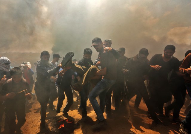 Los palestinos llevan a un manifestante herido durante los enfrentamientos con las fuerzas israelíes cerca de la frontera entre Gaza e Israel al este de la ciudad de Gaza el 14 de mayo de 2018, durante una manifestación el día en que la embajada de EE. UU. Se trasladara a Jerusalén. Estados Unidos traslada su embajada en Israel a Jerusalén el lunes luego de meses de protesta mundial, ira palestina y elogios exuberantes de los israelíes por la decisión del presidente Donald Trump de dejar de lado décadas de precedentes. Existe la preocupación de que las protestas de Gaza a menos de 100 kilómetros (60 millas) de distancia se vuelvan letales si los palestinos intentan dañar o cruzar la valla con francotiradores israelíes posicionados en el otro lado. / AFP PHOTO / MAHMUD HAMS