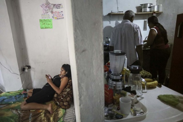 Venezuelan Carlos Figueroa (C) and another Venezuelan migrant cook as his daughter watches TV, in Medellin, Colombia, on April 18, 2018. Exiled Venezuelans have no expectations of the presidential election taking place next May 20 in their home country. / AFP PHOTO / JOAQUIN SARMIENTO