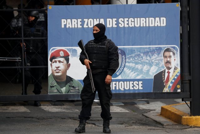 Members of the Bolivarian National Intelligence Service (SEBIN) stand guard next to a banner with the images of Venezuela's President Nicolas Maduro and Venezuela's late President Hugo Chavez, outside a detention center, where a riot occurred, according to relatives, in Caracas, Venezuela May 16, 2018. REUTERS/Carlos Garcia Rawlins