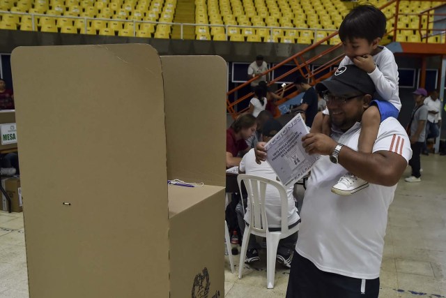 A man with his son votes at a polling station in Cali, Valle del Cauca Department, during presidential elections in Colombia on May 27, 2018. Voters went to the polls Sunday to choose a new president of Colombia in a divisive election that is likely to weigh heavily on the future of the government's fragile peace deal with the former rebel movement FARC. / AFP PHOTO / Luis ROBAYO